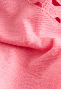 Rózsaszín pamutszövet közelről, lágy textúrával, finom bordázattal és hullámos szegélyrészlettel. Enyhén gyűrött megjelenés.