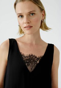 Schwarzes ärmelloses Top mit einem V-Ausschnitt und einem Spitzeneinsatz mit floralen Mustern am Ausschnitt. Weiche, glatte Textur.