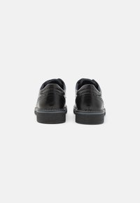 Chaussures en cuir noir avec un design texturé, finition lisse, bouts ronds et semelles en caoutchouc contrastantes. Dotées de détails brogue sur le talon et sur les côtés.