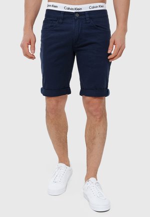 Mornarske pamučne šorts hlače s prevrnutim rubom, s prednjim zatvaranjem na gumb i elastičnom trakom s Calvin Klein logom. Nosite s bijelim tenisicama.