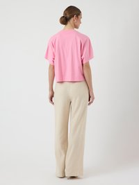 Un tricou scurt roz cu mâneci scurte și decolteu rotund, asociat cu pantaloni largi bej, amândouă dintr-un material fin.