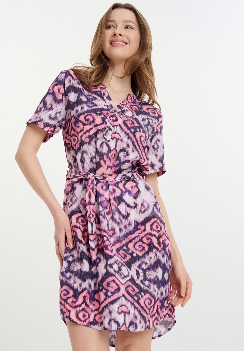 Kurzes Kleid mit kurzen Ärmeln, das ein lila, pinkes und weißes abstraktes Muster aufweist, einen V-Ausschnitt hat und an der Taille gebunden ist. Es besteht aus einem glatten Stoff.