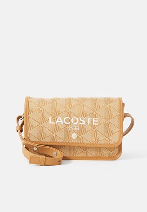 Bolso bandolera color bronce con patrón geométrico y texto blanco "LACOSTE 1933", con solapa y correa ajustable con tachuelas metálicas.