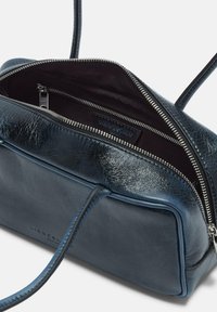 Sac à main en cuir bleu marine avec deux anses, fermeture éclair principale ouverte, poche intérieure zippée et nom de la marque embossé sur l'avant et à l'intérieur.