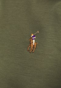 Olivgrön piké med en brun broderad logotyp av en polo-spelare och häst med färgglada accenter. Slät textur, klassisk passform.