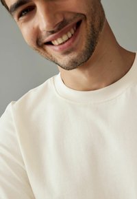 Cream-colored crew neck t-shirt made of soft cotton blend fabric; features a smooth texture and subtle stitching around the neckline.