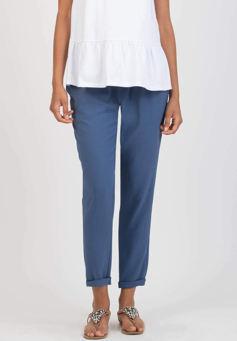 Blue tapered pants featuring a soft texture, roll-up cuffs, and a relaxed fit, paired with a white peplum top and embellished sandals.