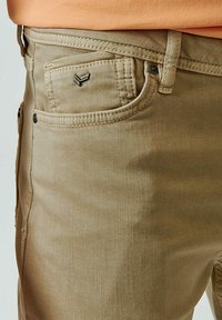 Beige katoenen broek met een front pocket en een klein metalen logodetail. Glad textuur en rechte pasvorm met zichtbare gestikte naden.