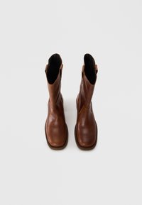 Bottes chelsea en cuir marron avec une finition lisse, des orteils ronds, des ouvertures sur le côté et une semelle texturée.