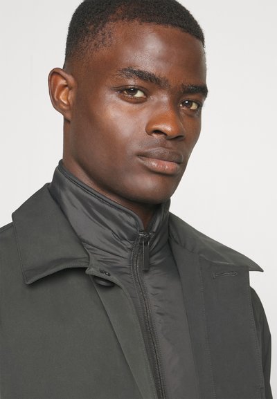 Chaqueta de abrigo negra con cuello alto y una capa interior en contraste, con textura suave y cierre frontal con cremallera.