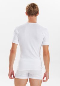 Hvid kortærmet t-shirt med rund hals, lavet af glat stof. Pasformen er tætsiddende, og den er kombineret med hvide shorts. Enkel, ren design.