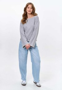 Gray long-sleeve top with white trim, paired with light blue wide-leg jeans and gray sneakers featuring black stripes. Simple design and relaxed fit.