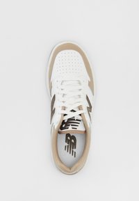 Vit sneaker med bruna accenter, med perforerat ovandel, platta snören och platt gummisula. Logotyp på sidan och mönstrad innervaddering.