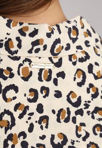 Tissu à imprimé léopard avec des couleurs noire, brune et crème ; détail de col ; étiquette métallique de marque avec le logo "Missounform".