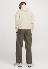 Crème hoodie met een trekkoordcapuchon, ontspannen pasvorm. Gecombineerd met olijfgroene broeken met twee achterzakken, gedragen met lichtgekleurde sneakers.