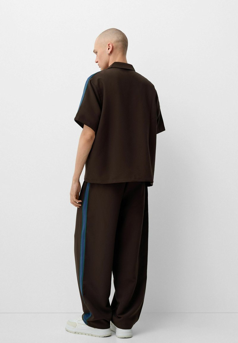 Polo marron à manches courtes et pantalon large assorti avec des bandes latérales bleues, fabriqué dans un matériau doux, avec une coupe décontractée et un design minimaliste.