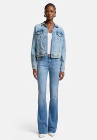 Veste en denim bleu clair avec poches avant, col classique et fermeture à boutons, assortie à un jean flare bleu clair et des talons blancs pointus.