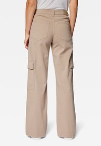 Beige weit geschnittene Cargo-Hosen mit aufgesetzten Taschen, Gürtelschlaufen und einer glatten Textur. Sichtbare Nähte auf der Rückseite und zwei Gesäßtaschen.
