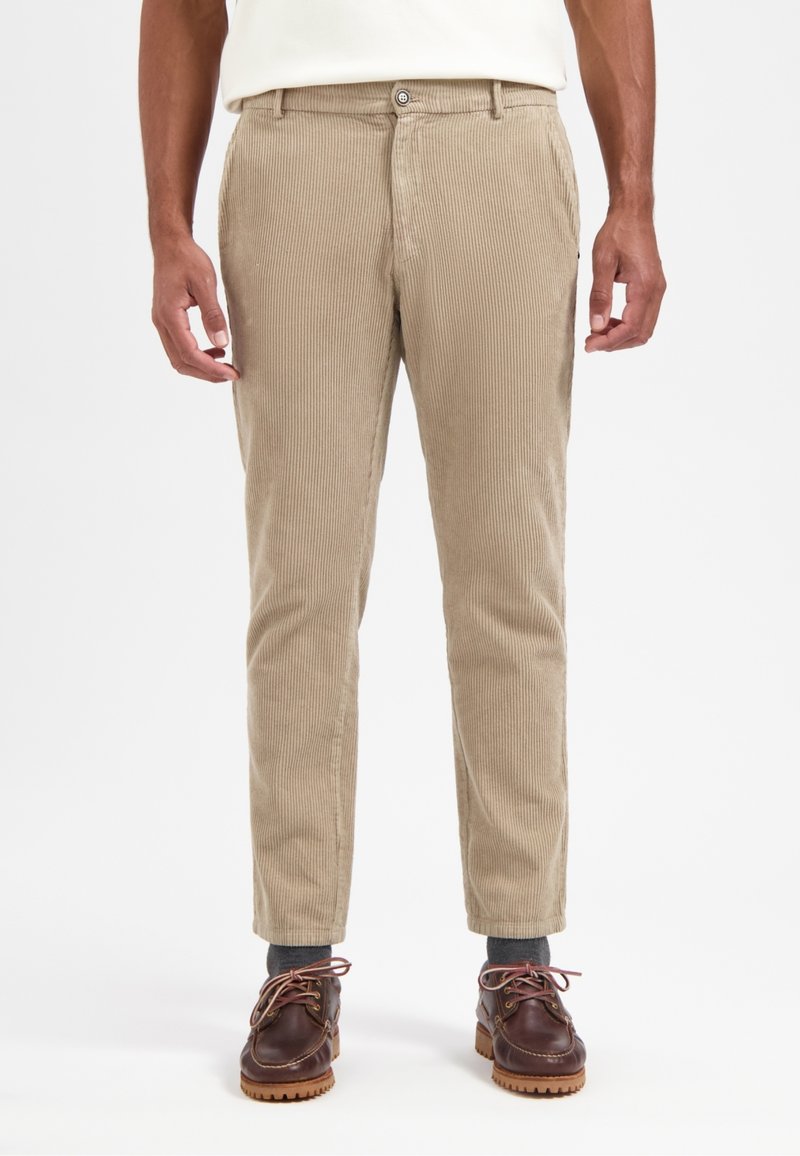 Beige Corduroyhose mit geradem Schnitt, vertikaler Rippung, Knopfverschluss und Seitentaschen. Getragen mit braunen Schuhen.