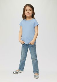 Helles blaues Baumwoll-T-Shirt mit kurzen Ärmeln und drei kleinen Herzverzierungen. Getragen mit blauen Jeans mit herzförmigen Taschen und silbernen Schuhen.