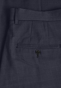 Mörkblå rutiga byxor med en mjuk textur; har en bakficka med en svart knapp och en subtil houndstooth-mönstring i tyget.