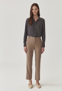 Navy button-up shirt with small, light-colored patterns; beige tailored trousers with front creases; light-colored slip-on shoes.