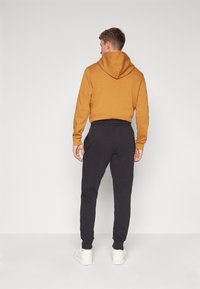Huvtröja i senapsgul, tillsammans med svarta sweatpants. Materialet verkar mjukt, med ribbade muddar och resårmidja.