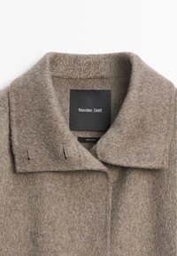 Brązowy wełniany płaszcz z klasycznym kołnierzem, z subtelną fakturą i detalami przeszyć. Etykieta z napisem "Massimo Dutti", made in China.