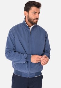 Giacca bomber blu con una texture liscia, polsini e orlo a costine, e una zip frontale. Design semplice e classico, adatto per un abbigliamento casual.