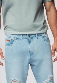 Jeans de mezclilla azul claro con un corte holgado, que presentan desgastes en las rodillas, cinco bolsillos y una etiqueta de piel de la marca en la cintura.