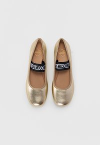 Guldmetalliska ballerina-tofflor med rund tå, svart elastisk rem med "LOVE MOSCHINO" och beige inredning. Slät textur.