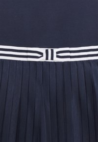 Námořnický šaty s hladkým, přiléhavým korzetem a skládací sukní. Obsahují bílý pas s námořnickými pruhy a mašlový detail.