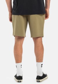 Olive green shorts in a soft fabric, featuring a mid-thigh length, straight cut, and no visible pockets or embellishments. Paired with black shoes and white socks.