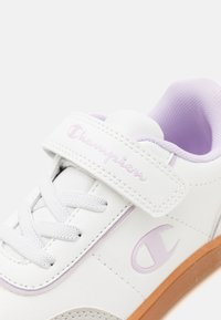 Białe sneakersy z liliowymi akcentami, z paskiem, okrągłym noskiem, teksturowaną podeszwą i detalem z logo. Gładki materiał syntetyczny z zapięciem na sznurówki.