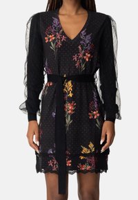 Black floral dress with a V-neck, long sheer sleeves, and polka dot pattern. Features colorful flowers, a fabric belt, and lace trim.