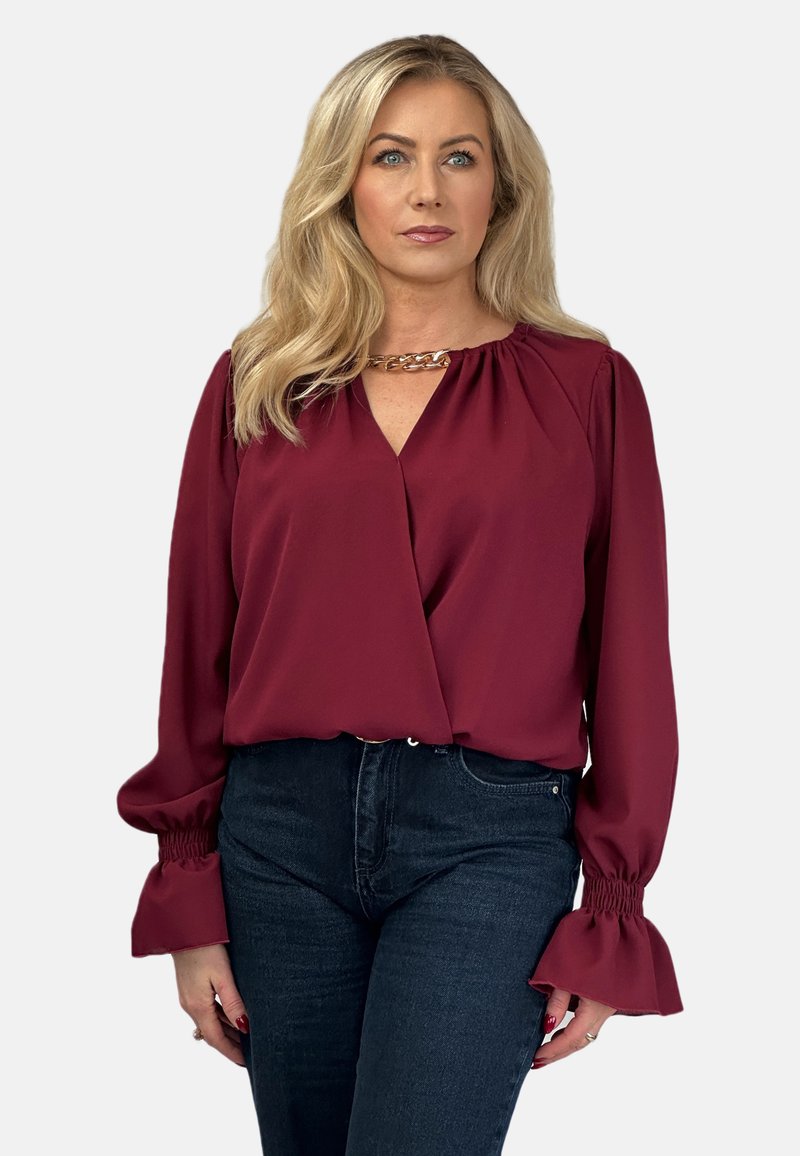 Burgundowa bluzka z długimi, bufkami rękawami i niskim dekoltem w kształcie litery V. Posiada marszczone detale przy dekolcie oraz elastyczne mankiety.