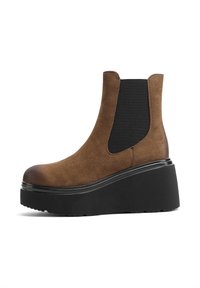 Stivaletto in suede marrone con pannelli elastici ai lati, punta arrotondata e una robusta suola nera a piattaforma, con una superficie testurizzata.