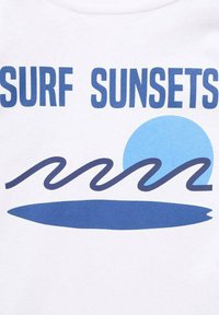 Biela tričko s modrým textom "SURF SUNSETS" nad štylizovaným modrým slnkom a vlnitým grafickým motívom mora, s horizontálnym tmavomodrým akcentom pod ním.
