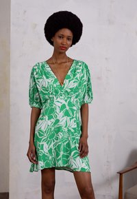 Vestido floral verde com decote em V, mangas bufantes e cintura elástica. Feito de um tecido leve com um padrão floral branco.