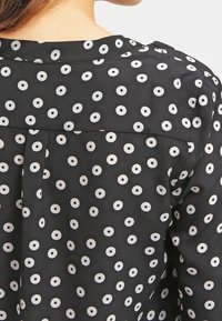 Blusa nera a fantasia con pois bianchi, in tessuto morbido e con un design a pieghe sul retro. Collo semplice e dettagli in texture liscia.