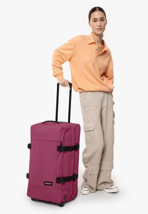 Maleta de ruedas púrpura con correas y herrajes negros, de forma rectangular, hecha de un material duradero. Asas para un transporte fácil.