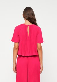 Fuchsia gefaltetes Oberteil mit rundem Halsausschnitt und kurzen Ärmeln. Mit einer Schlüssellochöffnung im Rücken. Glattes Material, lockerer Schnitt.