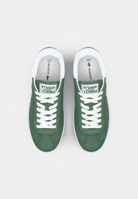 Gröna sportiga sneakers med vita snören och detaljer. Har en texturerad tygovandel, rund tå och ett märkesetikett på tungan.