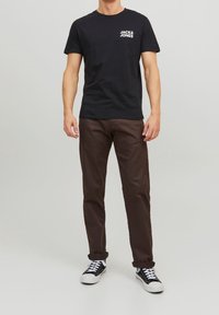 Musta puuvillainen t-paita, jossa valkoinen logo, yhdistetty ruskeisiin chinos-housuihin ja mustiin lenkkareihin, joissa valkoiset korostukset ja mustat nauhat.