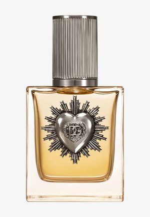 Flacon de parfum carré en verre avec liquide doré, emblème cœur argenté orné avec les initiales "DG", et bouchon métallique côtelé.