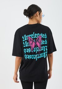 Black oversized t-shirt featuring a pink and purple dripping butterfly graphic and stylized turquoise text on the back. Cotton material.