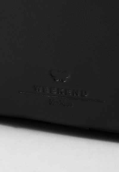 Melnas ādas aksesuārs ar iegravētu vārdu "WEEKEND" un tauriņa emblēmu. Gluda tekstūra ar matētu apdari un smalku zīmola detaļu.