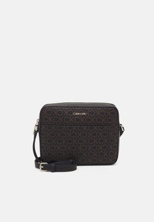 Rechthoekige zwarte Calvin Klein crossbodytas met bruin CK-logopatroon, gouden rits en verstelbare riem opgerold aan de voorkant.