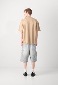 Tricou bej cu mânecă scurtă și guler rotund, combinat cu pantaloni scurți cargo gri deschis, cu buzunare laterale și o textură uzată. Pantofi negri și șosete albe.