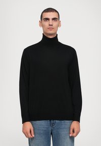 Svart polo-tröja med långa ärmar, ribbad textur och avslappnad passform, matchad med ljusblå jeans.